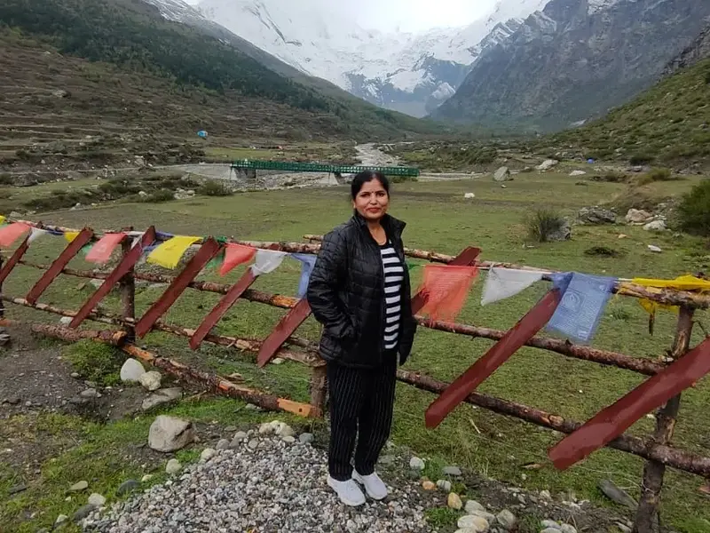 Rekha on her last trip, standing by prayer flags in a green Himalayan valley